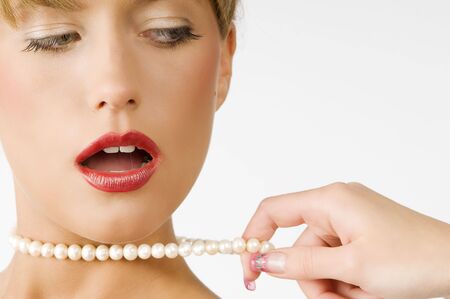 portrait of a cute girl with red lips and pearls necklace pulling by one handの写真素材