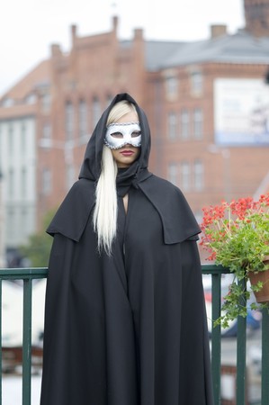 outside portrait of pretty blond with white mask and black cloak with hood