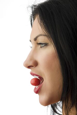 one side shot of a beautiful brunette with red lips and a red candy between teethの写真素材