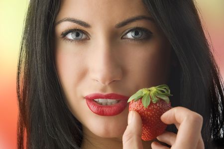 beautiful portrait of cute brunette girl with strawberry near her faceの写真素材