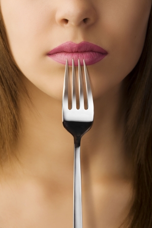 close up of woman mouth with pink lipstick keeping a fork near the lipsの写真素材