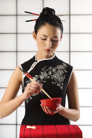 beautiful asian girl in calssic oriental dress in act to eat with chopstickの写真素材