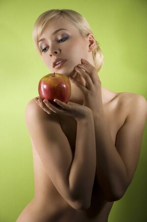 fashion and glamour shot of a dreaming nude young woman with red apple on green background の写真素材