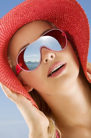 fine portrait of young cute woman with red summer hat and sun glasses looking at the sea in a sunny dayの写真素材