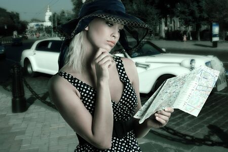 elegant woman in blue polka dot dress and hat looking at a tourist map の写真素材