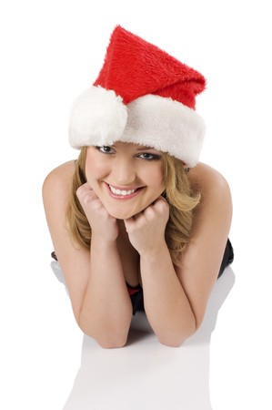 close up portrait of a blond cute girl wearing a christmas hat and laying down on a white floor looking in camera wirh a smileの写真素材