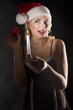 cute and attractive young woman with nightgown and a christmas hat shaking a little giftの写真素材