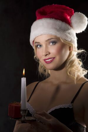 smiling and cute attractive young woman with nightgown ant a christmas hat in the dark with a candle looking in cameraの写真素材