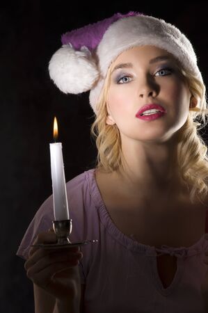 cute and attractive young woman with pink nightgown ant a christmas hat looking in the dark with a candle の写真素材