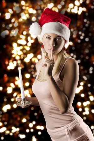 beautiful young woman wearing a christmas hat and keeping a candle in a dark contest in act to shut up peopleの写真素材