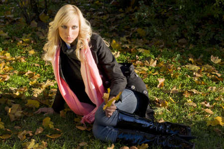 warm and fashion portrait of blond model sitting on the grass in a sunny winter day with hair styleの写真素材