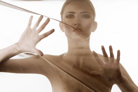 art fashion portrait of naked woman behind transparent material looking in cameraの写真素材