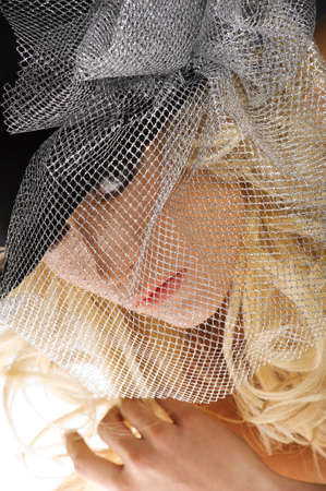 close up portrait of cute blond woman looking in camera with a silver net cover her faceの写真素材