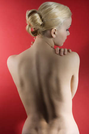 fashion elegant shot of blond naked woman with hair styliss taking pose on red backgroundの写真素材