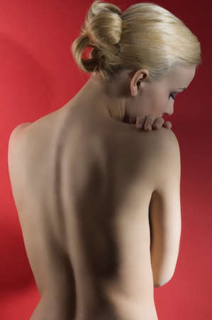 fashion elegant shot of nude blond woman with hair stylish taking pose on red backgroundの写真素材