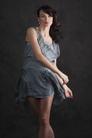 portrait of trendy young woman in elegant blue dress posing against black backgroundの写真素材
