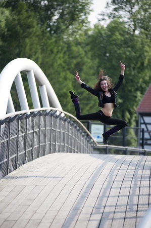 young and happy pretty woman jumping for joy on a white bridge outdoorの写真素材