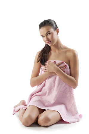 beautiful young brunette covering her naked body with a pink bath towel sitting down on white floorの写真素材