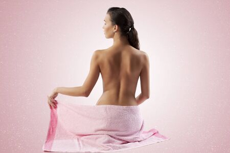 naked brunette showing her back shoulder and covering her body with a pink towelの写真素材
