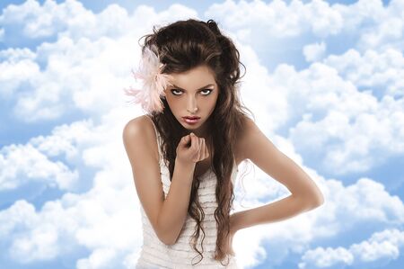 fashion shoot of a curly brunette wearing a white dress and a pink feather in her hairの写真素材