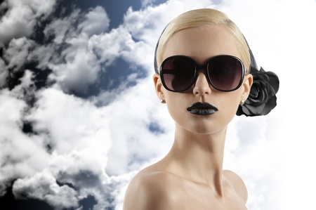 fashion portrait of young blond woman with hair style black lips and wearing sunglasses looking at the camera against white backgroundの写真素材