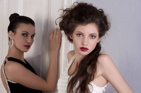 two beautiful women with hair style and elegant dress posing indoor near an old fashion door looking...