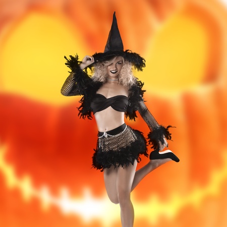 glamour shot of a cute and curled blonde posing in a black witch costume and high heelsの写真素材