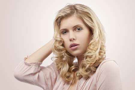 fresh and pretty young girl wearing a pink shirt and with curly hairstyle on her blond long hair looking at the camera with lovely pose against white backgroundの写真素材