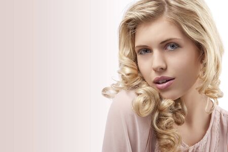 fresh and pretty young girl wearing a pink shirt and with curly hairstyle on her blond long hair and beautiful face looking at the camera with attractice pose against white backgroundの写真素材