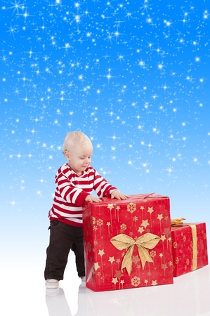 sweet and funny shot of a baby boy in red t-shirt playing with two big christmas gift box. He is standing near the big gift box and has the hands on thatの写真素材