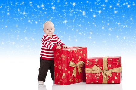 sweet and funny shot of a baby boy in red t-shirt playing with two big christmas gift box. He is standing near the big box and looks in to the lens.の写真素材