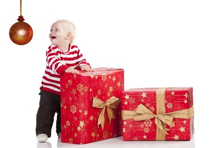 sweet and funny shot of a baby boy in red t-shirt playing with two big christmas gift box. He is standing near the big box and looks on the left .の写真素材