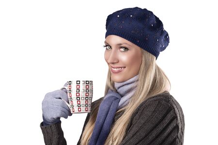 pretty blonde wearing warm winter clothes in grey and blue holding a hot cup of tea and smilingの写真素材