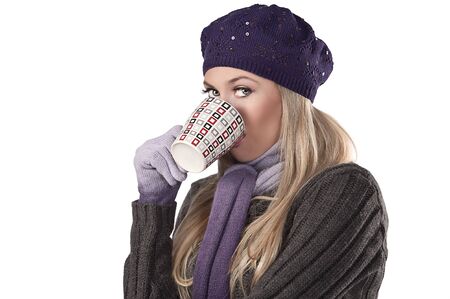 beautiful and natural blonde girl holding a hot cup of tea wearing a purple knitted cap and scarf and glovesの写真素材