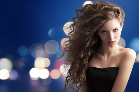 beauty fashion portrait of a very young cute brunette with long curly hair with hairstyle flying in the wind on bokeh backgroundの写真素材