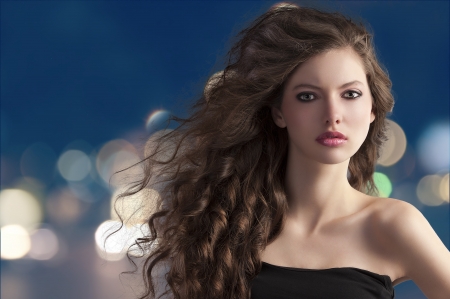 beauty fashion portrait of a very young cute brunette with long curly hair with hairstyle flying in the wind on city light bokehの写真素材