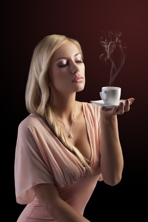 sensual blond girl with hair style holding a  coffee set in elegant pink dress over dark fashion backgroundの写真素材