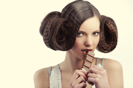 very young pretty girl with creative hairstyle eating a tablet of chocolate wearing a old style dress
の写真素材