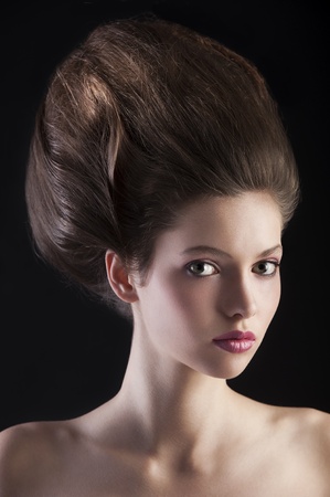 close up portrait of young beautiful girl with dark hair and creative hairstyle posing over black backgroundの写真素材