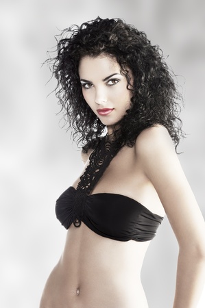 young and very beautiful brunette with curly hair and deep red lips wearing a fashion black swimsuit and jewelleryの写真素材