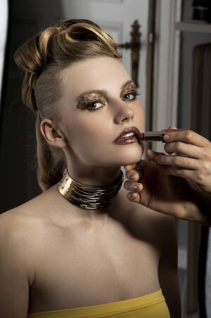 fashion portrait of cute and elegant lady doing make up on backstage with spot light on her faceの写真素材
