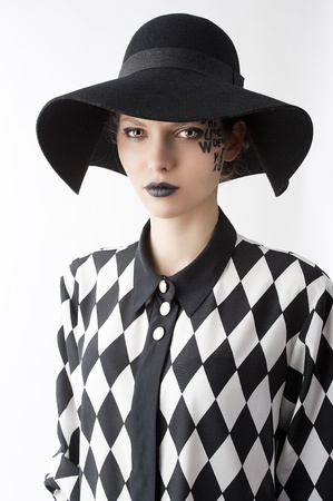 pretty and beautiful young lady with a creative make up made with letter on face and black hat and unusual shirt, she is in front of the camera and looks in to the lens with serious expressionの写真素材