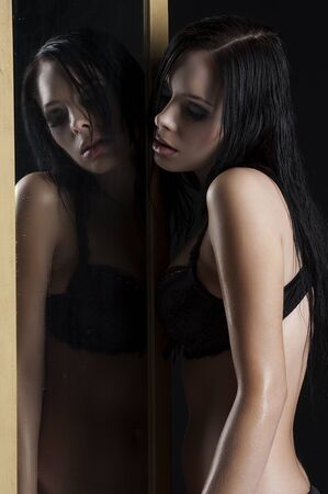 sexy and beautiful brunette in black lingerie looking through a dropped mirror with wet hair の写真素材