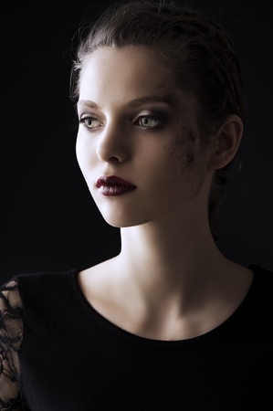 close up portrait of very beautiful young lady actrees over a dark background with dirty make up and fashion light, she is turned of three quarters at right and looks in front of herの写真素材