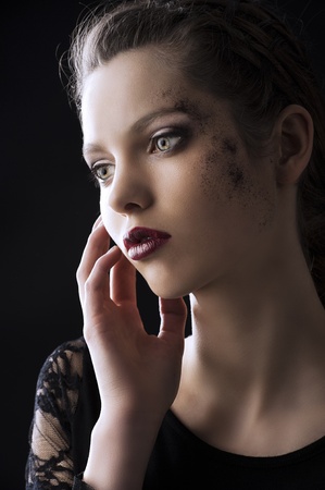 close up portrait of very beautiful young lady actrees over a dark background with dirty make up and fashion light, she is turned of three quarters at right, she looks in front of her and her right hand is near the faceの写真素材