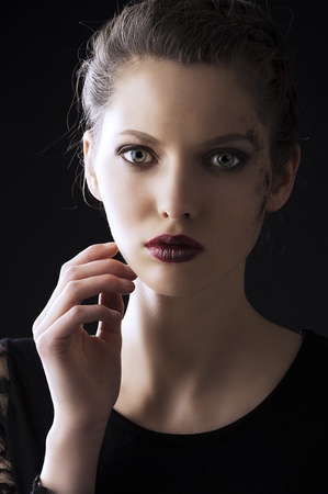 close up portrait of very beautiful young lady actrees over a dark background with dirty make up and fashion light, she is in fornt of the camera, looks in to the lens and her right hand is near the faceの写真素材
