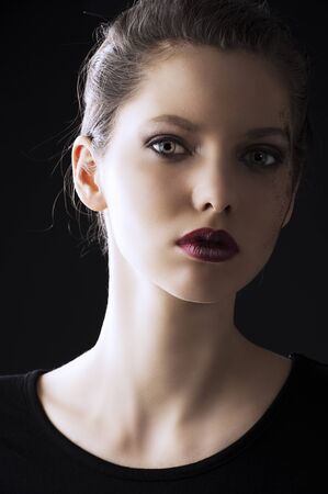 close up portrait of very beautiful young lady actrees over a dark background with dirty make up and fashion light, she is slightly turned of three quarters at left and she looks in to the lens with intense expressionの写真素材