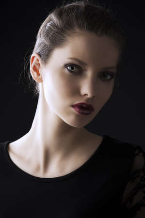 close up portrait of very beautiful young lady actrees over a dark background with dirty make up and fashion light, she is turned of three quarters at left and she looks in to the lens with intense expressionの写真素材