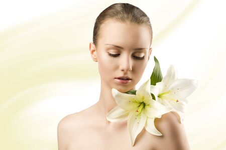 beauty portait of pretty young girl with lilies, she is slightly turned of three quarters at left and looks lilies on her left shoulderの写真素材