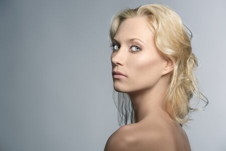 beautiful blonde girl with nudes shoulders and natural makeup, turned of three quarters at right and looks in to the lensの写真素材